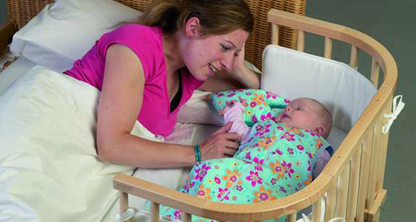 Mutter mit Baby im Bett neben dem Babybett